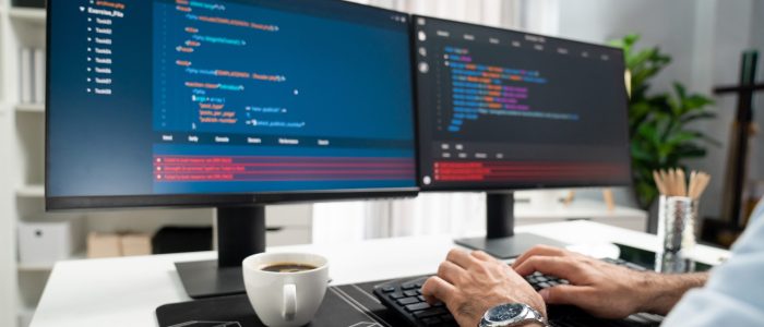 Cropped typing hands photo in smart IT developer working software development coding on two pc creating virus firmware application program version on website with coffee cup at modern office. Surmise.
